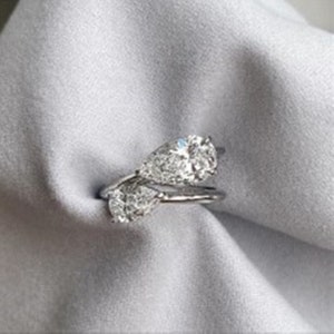 以下が含まれることがあります： ねじれたバンドにセットされた、2つの洋梨型の透明な石が付いたシルバーリングです。