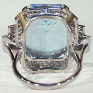 May include: A silver ring with a large, rectangular aquamarine gemstone surrounded by a halo of smaller diamonds.