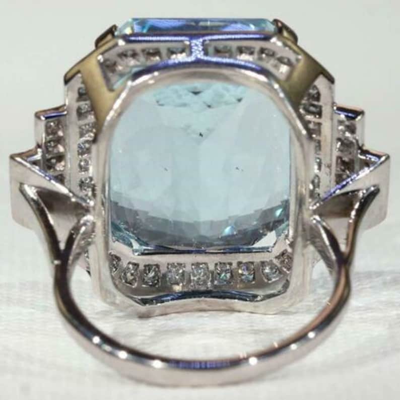 May include: A silver ring with a large, rectangular aquamarine gemstone surrounded by a halo of smaller diamonds.