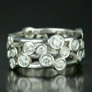 Puede incluir: Un anillo de banda de plata con un racimo de diamantes redondos engastados en bisel. Los diamantes están dispuestos en un patrón escalonado, creando un diseño único y llamativo.