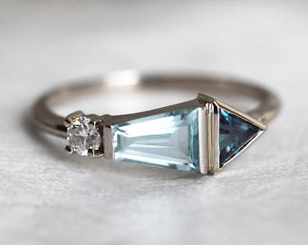 May include: A silver ring with a triangular aquamarine gemstone, a smaller round diamond, and a smaller triangular blue topaz gemstone.