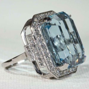 May include: A silver ring with a large, light blue aquamarine gemstone surrounded by a halo of smaller diamonds.