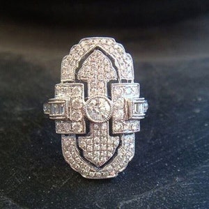 May include: A silver ring with a large, intricate design featuring a central diamond and smaller diamonds set in a geometric pattern.