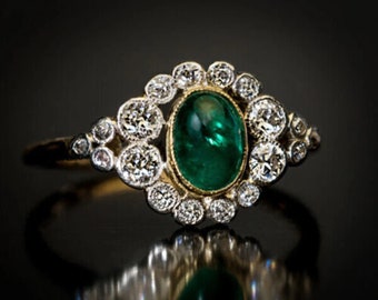 May include: A vintage emerald and diamond ring. The ring features a large, oval-shaped emerald set in a gold bezel. The emerald is surrounded by a halo of smaller diamonds. The ring is made of white gold and yellow gold.