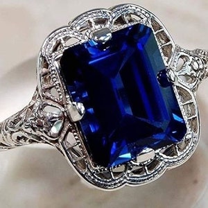 May include: A silver ring with a large, deep blue, emerald-cut gemstone set in a filigree design.