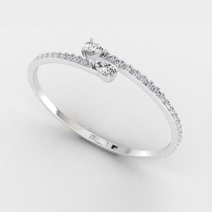 Könnte beinhalten: Ein silbernes Armband mit filigranem Design. Das Armband hat eine Reihe kleiner, klarer Edelsteine entlang des Bandes, mit zwei größeren, birnenförmigen Edelsteinen oben. Das Armband ist vor einem weißen Hintergrund platziert.