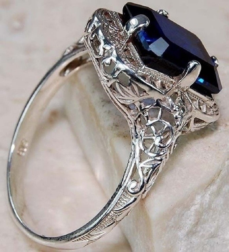 May include: A silver ring with a large, dark blue gemstone set in a filigree design.