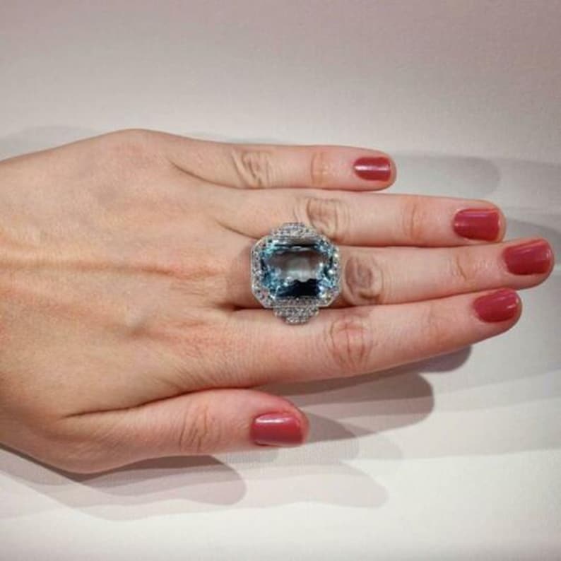 May include: A large, rectangular aquamarine gemstone ring set in silver with a halo of smaller diamonds.