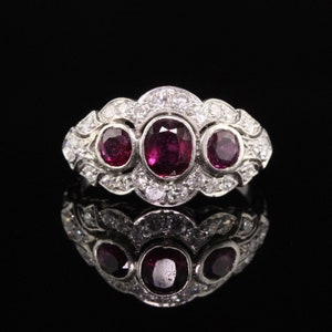 May include: A silver ring with three ruby gemstones and a diamond halo setting.