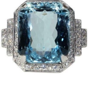 May include: A large, light blue aquamarine gemstone ring set in a silver band. The aquamarine is surrounded by a halo of smaller diamonds.