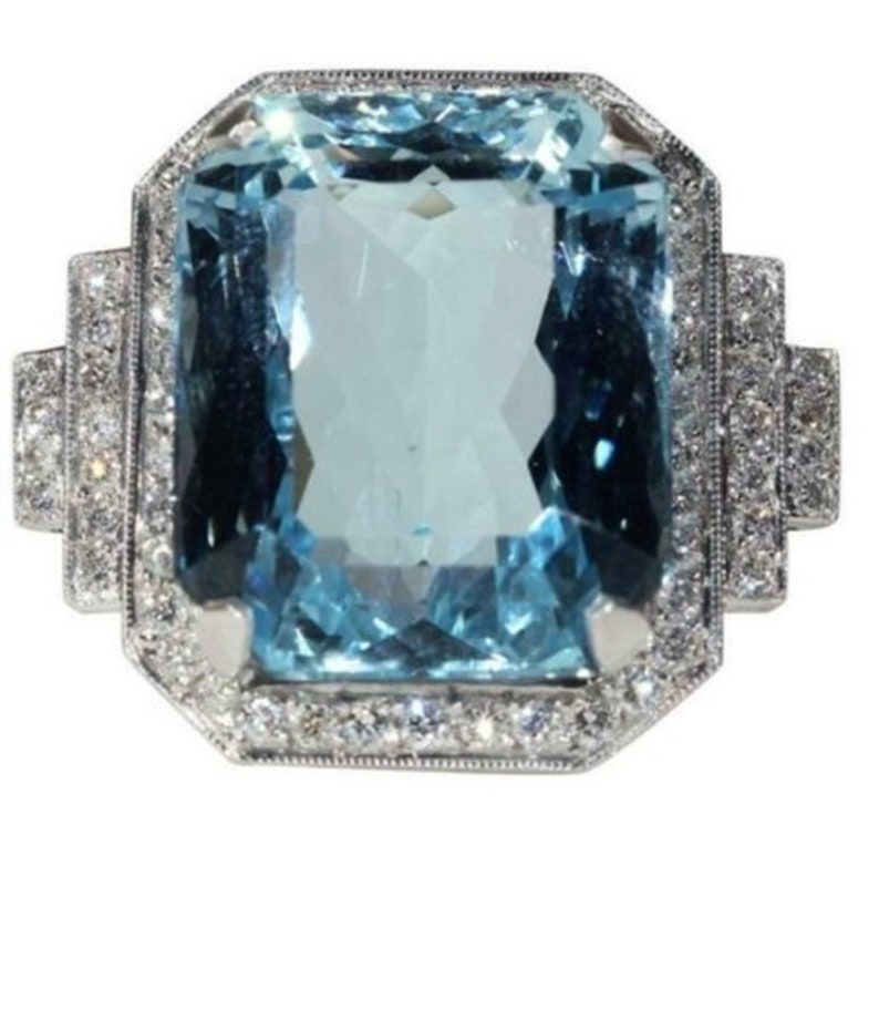 May include: A large, light blue aquamarine gemstone ring set in a silver band. The aquamarine is surrounded by a halo of smaller diamonds.