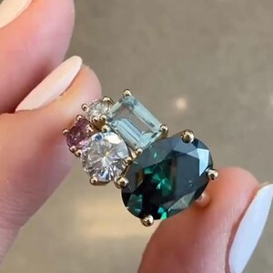May include: A gold ring with a large oval green gemstone surrounded by smaller gemstones in shades of blue, pink, and white.