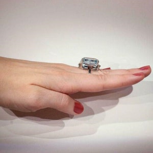 May include: A silver ring with a large, rectangular aquamarine gemstone surrounded by smaller diamonds. The ring is set on a white background.