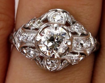 May include: A vintage platinum engagement ring with a large round brilliant cut diamond surrounded by smaller diamonds in a delicate floral design.