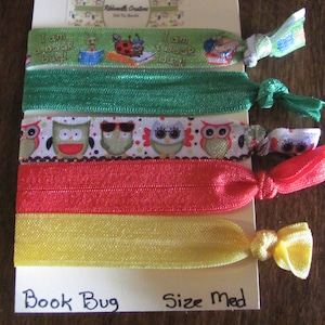May include: Set of four colorful hair ties with different designs. The hair ties are green, red, yellow, and white with owl and book bug patterns. The text "I am a book bug!" is printed on the green hair ties. The text "Book Bug" and "Size Med" is printed on the bottom of the card.