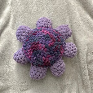 May include: A purple and pink crocheted plush toy shaped like a flower with eight petals.