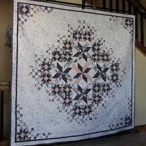 May include: A large, square quilt with a starburst design. The quilt features a central star pattern in shades of black, tan, and cream, surrounded by smaller star motifs. The background is a marbled cream color, and the quilt is bordered with a dark gray trim.