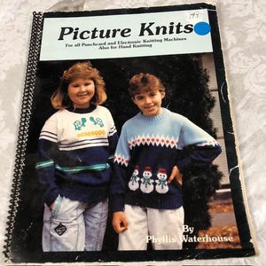 May include: A book titled "Picture Knits" for all punchcard and electronic knitting machines, also for hand knitting. The cover features two children wearing sweaters with knitted designs. The boy is wearing a blue sweater with a snowman design and the girl is wearing a white sweater with a turtle design.