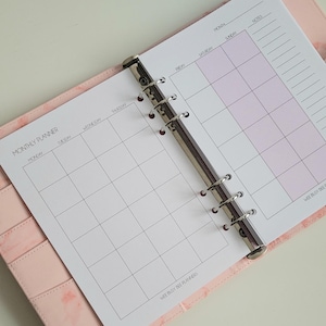 May include: A white monthly planner with a pink cover. The planner has a ring binder and is divided into days of the week. The planner has the text "MONTHLY PLANNER" and "WEE BUSY BEE PLANNERS" printed on it.