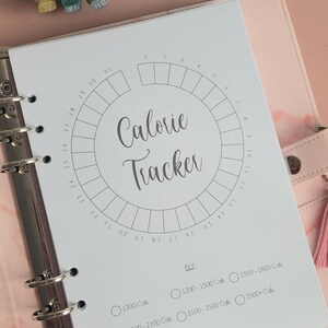 Peut inclure: Un suivi calorique imprimable avec un cercle divisé en 31 sections. Les sections sont numérotées de 1 à 31. Le cercle est intitulé "Calorie Tracker". Il y a quatre boutons radio sous le cercle avec les étiquettes suivantes : "1200 Cals", "1200-1500 Cals", "1500-1800 Cals", "2100-2500 Cals", et "2500+ Cals".