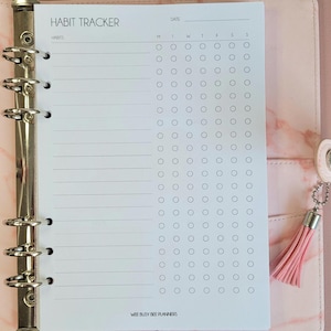 May include: A white habit tracker page with the title "Habit Tracker" and the words "Wee Busy Bee Planners" at the bottom. The page is divided into sections for "Habits" and days of the week, with circles for marking habits.