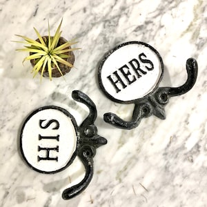 May include: Two black cast iron hooks with white porcelain signs that say "HIS" and "HERS".
