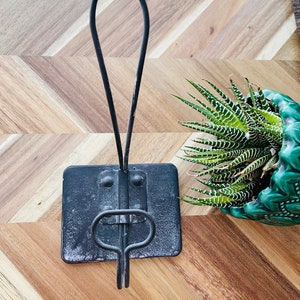 May include: Black metal towel rack with a square base and a curved hook. The rack is made of metal and has a rustic finish.