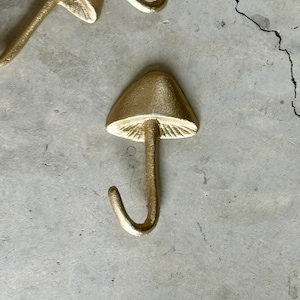 May include: Two gold mushroom-shaped hooks with a decorative design. The hooks are made of metal and have a matte finish.