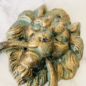 May include: A green and gold lion's head door knocker with a ring handle. The knocker is made of cast metal and has a distressed finish.