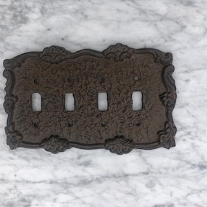 May include: A dark brown cast iron light switch plate with a decorative floral design and five switch openings.