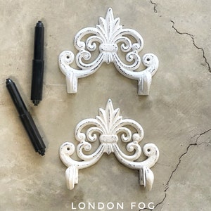 May include: Two white cast iron wall hooks with a decorative scroll design. The top hook is labeled "FLAT WHITE" and the bottom hook is labeled "LONDON FOG".