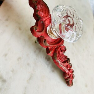 Puede incluir: Un tirador de armario vintage rojo y transparente. Presenta una base roja ornamentada y un pomo de cristal transparente. La pintura roja muestra signos de desgaste, lo que le da un encanto antiguo. Ideal para a&ntilde;adir un toque vintage a los muebles. Medidas en cm.