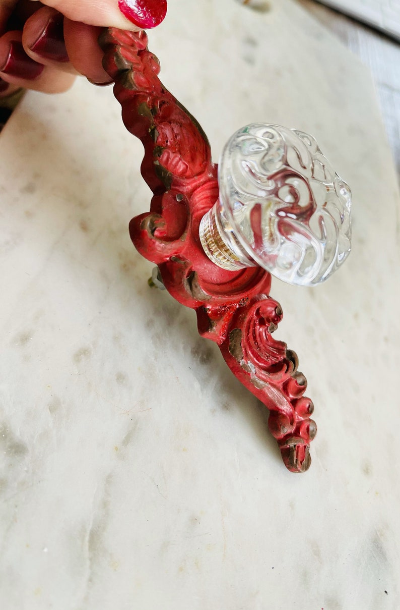 Puede incluir: Un tirador de armario vintage rojo y transparente. Presenta una base roja ornamentada y un pomo de cristal transparente. La pintura roja muestra signos de desgaste, lo que le da un encanto antiguo. Ideal para a&ntilde;adir un toque vintage a los muebles. Medidas en cm.