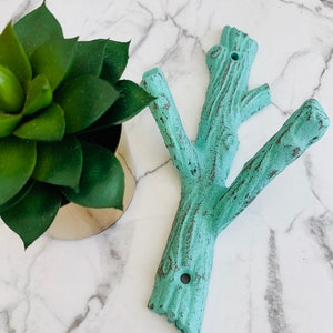May include: A turquoise blue metal wall hook shaped like a tree branch with three hooks. The hook is designed to look like a rustic tree branch with a distressed finish.