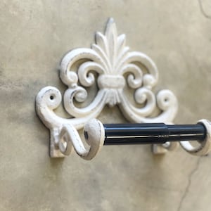 May include: White cast iron toilet paper holder with a decorative scroll design and a black metal rod.