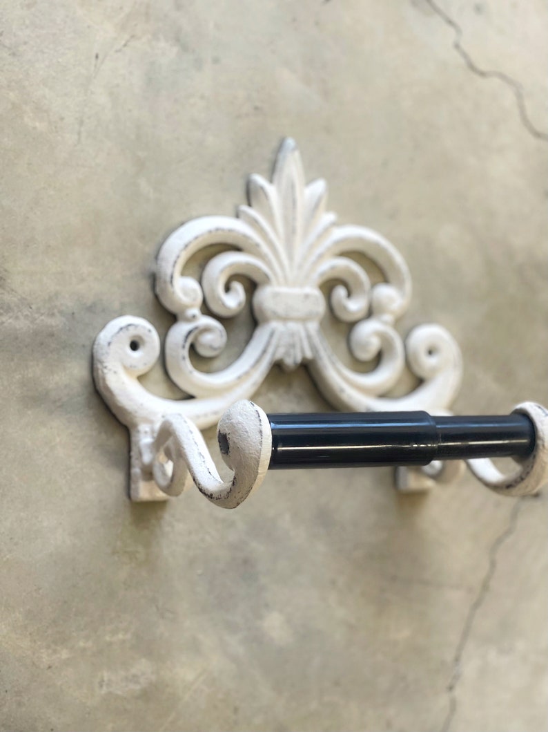 May include: White cast iron toilet paper holder with a decorative scroll design and a black metal rod.