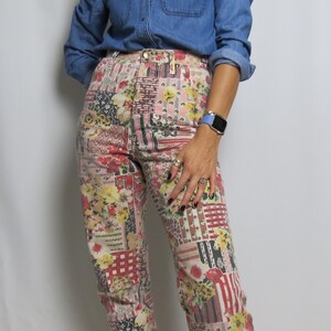 Op de afbeelding: Hoog getailleerde jeans in patchwork-stijl met een bloemen- en geometrisch patroon in rood, geel, roze en wit. De jeans wordt gecombineerd met een blauw spijkeroverhemd. De broek heeft een knoop- en ritssluiting.