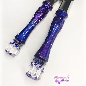 May include: A cake knife and server set featuring metallic silver blades and handles finished in a deep purple glitter coating with white polka dot accents and clear, faceted glass-like ends. The text Maryana's Bridal is printed in purple.