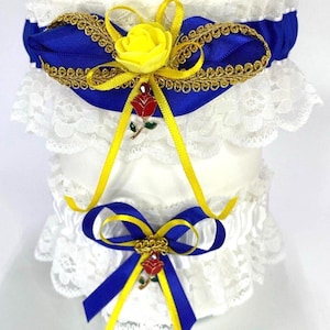May include: A white lace garter with blue satin ribbon, gold trim, and yellow accents. Features a yellow rose and a red rose charm. The garter is designed with a bow and ribbon detail.