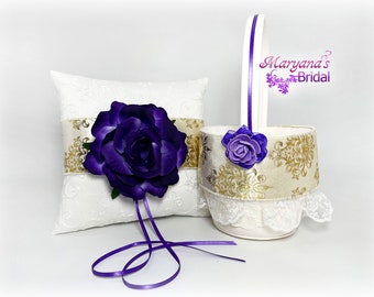 May include: A white ring pillow and a matching basket set featuring gold damask ribbon accents, deep purple fabric roses, and white lace trim. The pillow has two purple ribbon ties, and the basket has a white handle with a purple stripe. Text reads Maryana's Bridal.