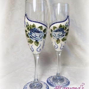 Puede incluir: Dos copas de champán decoradas con rosas azules y purpurina blanca y plateada. Las copas están sobre un fondo blanco con el texto "Maryana's Bridal" en morado.