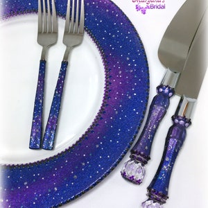 May include: A white plate with a wide, glittery purple and blue galaxy-patterned rim, two forks with matching glittery handles, and a cake knife and server set with decorative purple and blue handles featuring the text Maryana's Bridal.