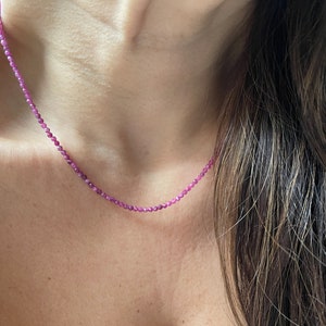 May include: A delicate pink gemstone necklace with small, round beads. The necklace is worn by a person with long brown hair.