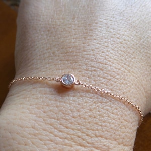 May include: A delicate rose gold chain bracelet with a single clear round gemstone.