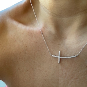 May include: A silver necklace with a diamond-encrusted cross pendant. The cross is set on a thin, curved bar.