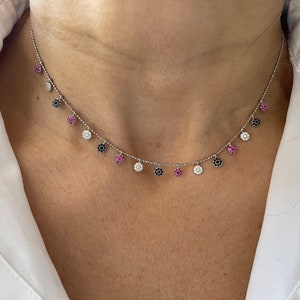 Puede incluir: Un delicado collar de cadena de plata con colgantes. Cada colgante es un pequeño círculo engastado con piedras preciosas blancas, negras y rosas.