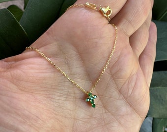 May include: A gold chain necklace with a small green cross pendant. The cross is made of tiny green gemstones.
