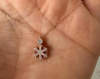 以下が含まれることがあります： クリアなキュービックジルコニアの石で飾られた雪の結晶のペンダントが付いた、繊細なローズゴールドのネックレスです。