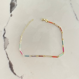 May include: A gold chain necklace with colorful enamel accents. The chain is made of small, rectangular links with a variety of colors, including red, pink, green, and blue.