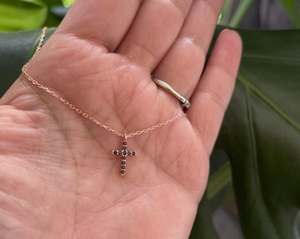 May include: A delicate gold chain necklace with a small black diamond cross pendant.